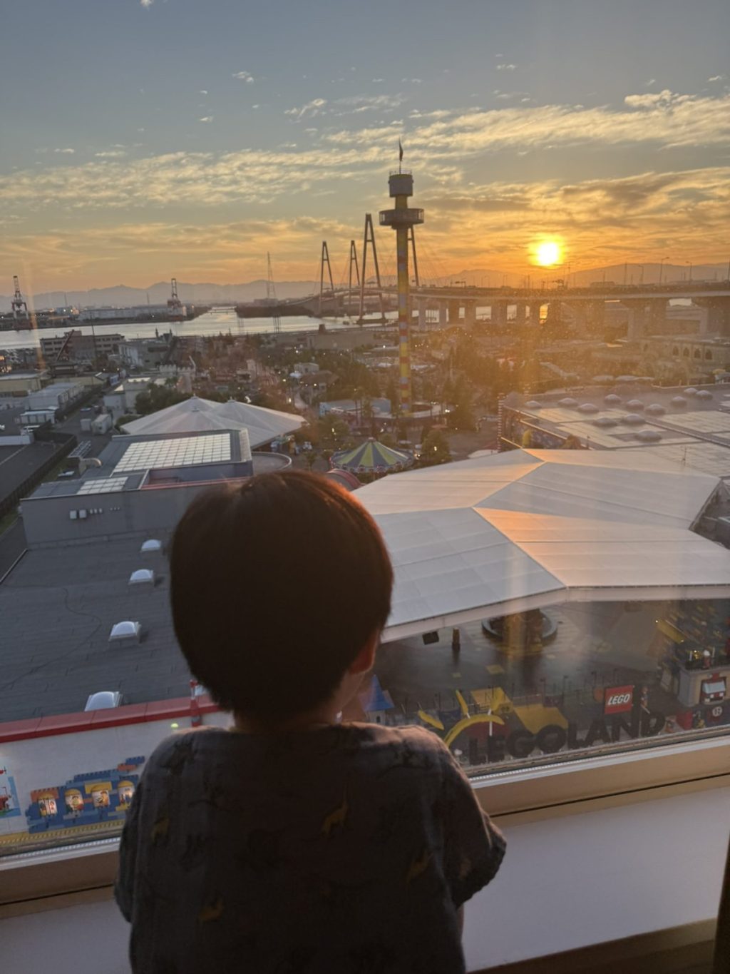部屋の窓から見えるレゴランドと夕日を眺める子ども